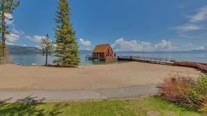 A beach with a wooden pier and a small building, likely a lodge or cabin, near a lake with mountains in the background.
