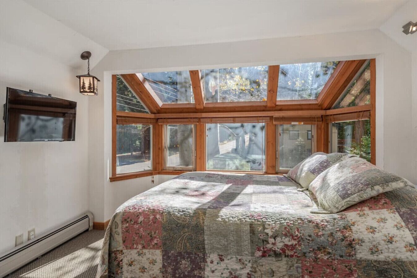 Un dormitorio con un tragaluz grande, una cama con colcha floral y un farol colgante.