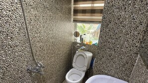 Un baño con pared de piedra texturizada, inodoro, lavabo y ventana con persianas.