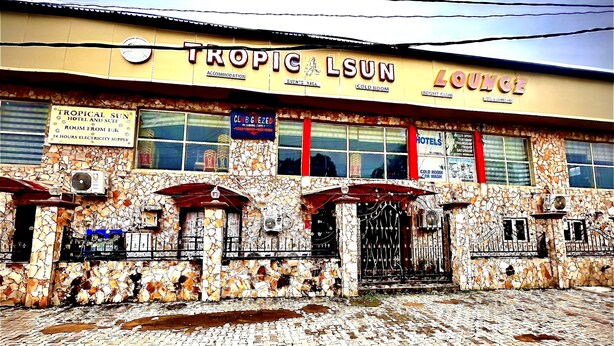 A building with a sign reading "TROPIC SUN HOTEL AND SIGHT ROOM FROM 24 HOURS ELECTRICITY SUPPLY".