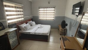 Un dormitorio con una cama, un escritorio, una silla, un televisor y dos ventanas con persianas.
