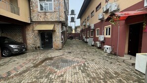 Un patio con un sendero empedrado, edificios de piedra y coches estacionados.