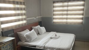 Una cama bien hecha con sábanas blancas, un cabecero de madera y una mesita de noche con un mueble decorado.