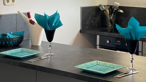 Eine moderne Küche mit zwei Pendelleuchten, einem Weinglas und einer Vase mit blauen Servietten.