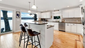 Une cuisine moderne dotée d’un grand îlot central, de meubles blancs et offrant une vue sur le lac.