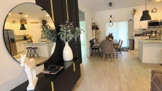 A modern living room with a black console table, a round mirror, and a dining area with a table and chairs. - Peaceful Ocala Home • Fire Pit • 20 Min to World Equestrian Center (Ocala)