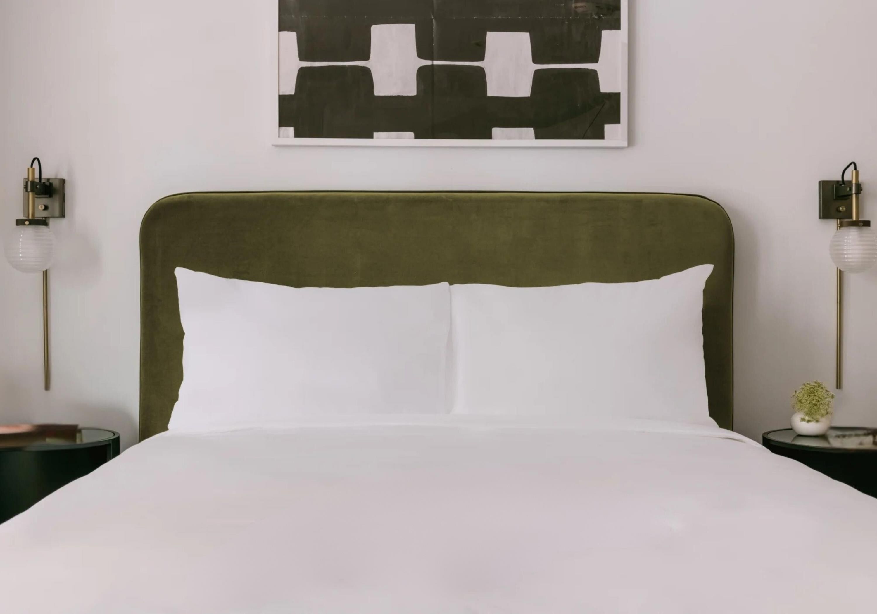 Una cama con cabecera tapizada en verde, ropa de cama blanca y dos mesitas de noche con lámparas.