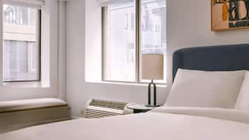 A hotel room with a large bed, a bedside table with a lamp, a heater, and a window with blinds.