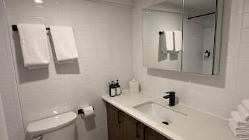 A modern bathroom with white tiles, a toilet, a sink, a mirror, and two towels on the wall.