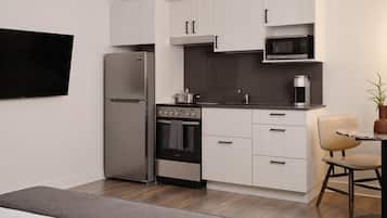 A compact kitchen with a refrigerator, oven, microwave, and a small dining area with a chair and table.