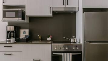 A modern kitchen with white cabinets, a stainless steel refrigerator, a microwave, a coffee maker, and a stove.