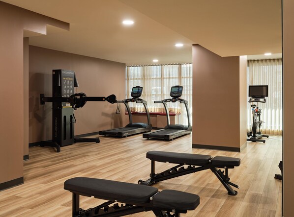 Een sportschool met loopbanden, een hometrainer en gewichtbanken.