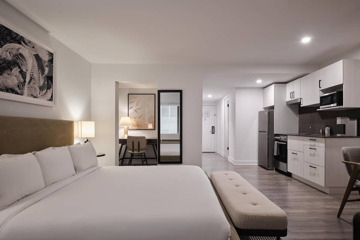 Una habitación de hotel moderna con una cama grande, un escritorio, una silla y una kitchenette.