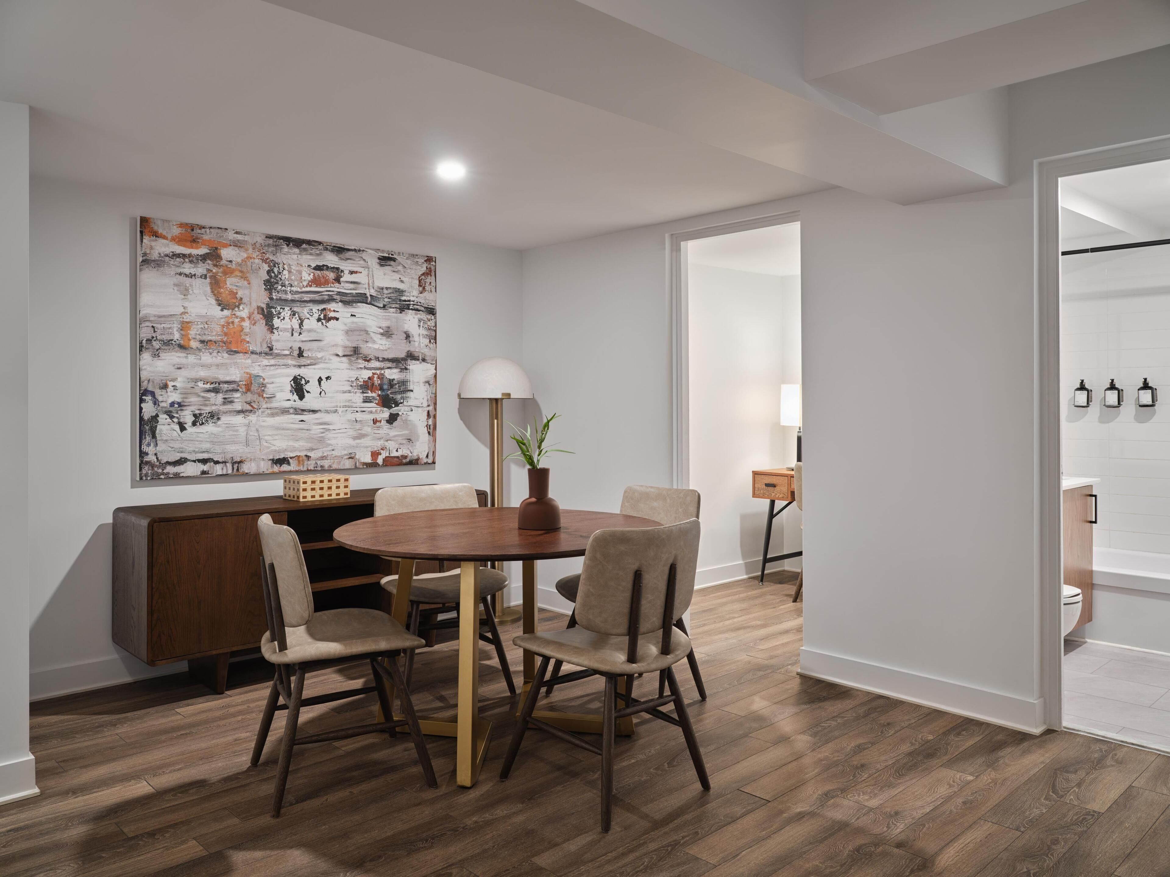 Un espace repas moderne avec une table ronde en bois, quatre chaises, une plante en pot et un grand tableau abstrait accroché au mur.