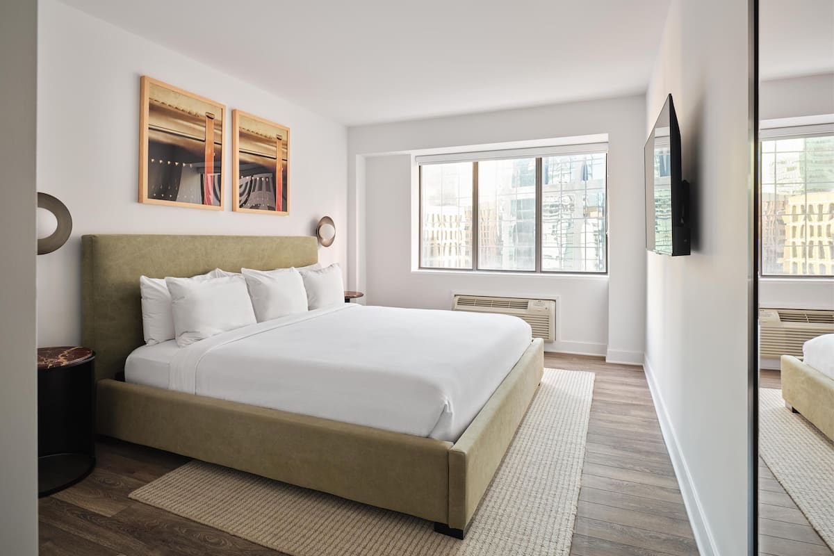 Un dormitorio moderno con una cama grande, una ventana con vista a la ciudad y obras de arte en la pared.