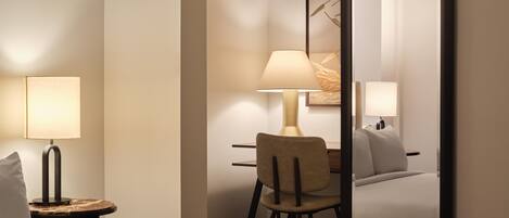 A hotel room with a bed, a desk with a chair, a lamp, and a large mirror.