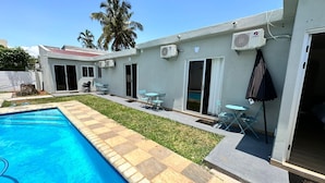 A swimming pool with a tiled edge, a grassy area, and a patio with chairs and a table.