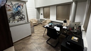 A modern office space with a desk, two chairs, a computer, and a painting on the wall.