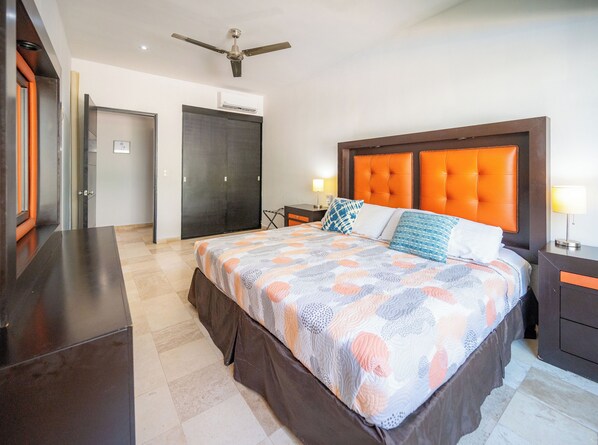 Habitación de hotel con cama, mesita de noche, lámpara, ventilador de techo y armario.