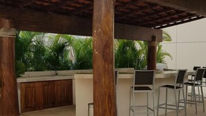 An outdoor patio with a wooden pergola, a bar area, and several chairs.