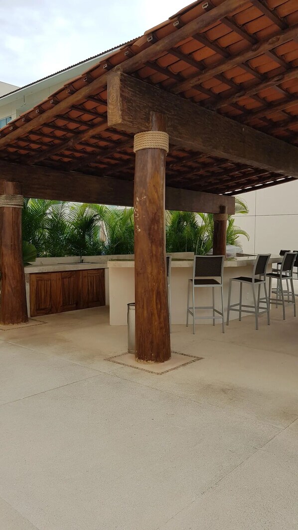 An outdoor patio with a wooden pergola, a bar area, and several chairs. - Amplio Departamento Ideal Para Pasar el Invierno o un Buen Verano (Ixtapa Zihuatanejo)