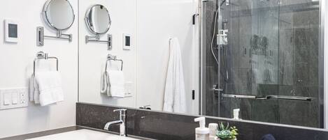 Een moderne badkamer met een grote spiegel, twee ronde spiegels, een witte wastafel, een douche en een handdoekhouder.