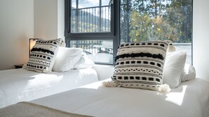 A bedroom with two beds, each with white bedding and patterned pillows. A large window with a view of trees and a mountain is visible. - Mountainview Escape Revelstoke Vacations (Revelstoke)