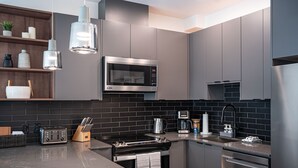 A modern kitchen with stainless steel appliances, a black tiled backsplash, and wooden shelves. - Mountainview Escape Revelstoke Vacations (Revelstoke)