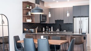 A modern kitchen with a central island, black and grey cabinetry, and a dining area with black chairs. - Mountainview Escape Revelstoke Vacations (Revelstoke)