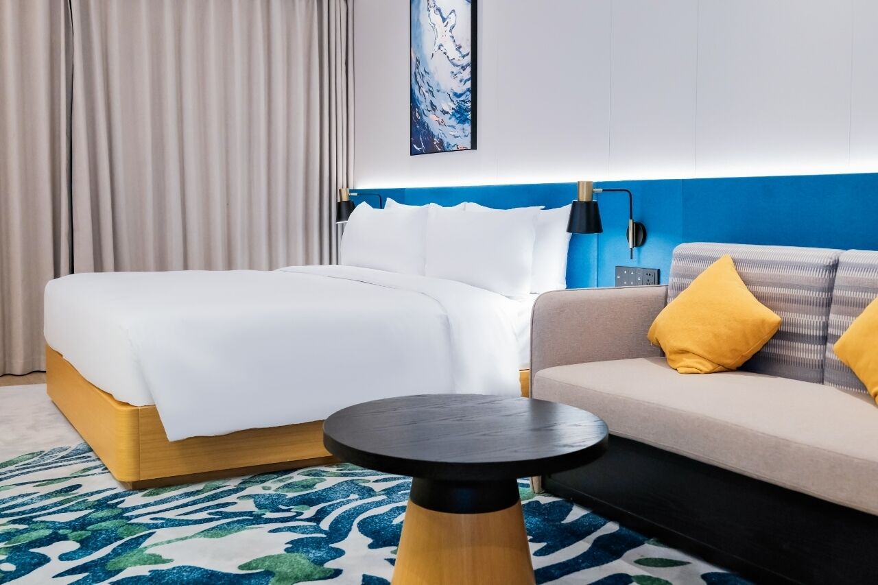 A hotel room with a bed, a sofa, a round table, and a wall-mounted lamp.