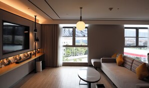 Una sala de estar moderna con un televisor grande, un sofá, una mesa de centro y vistas de la ciudad a través de amplias ventanas.