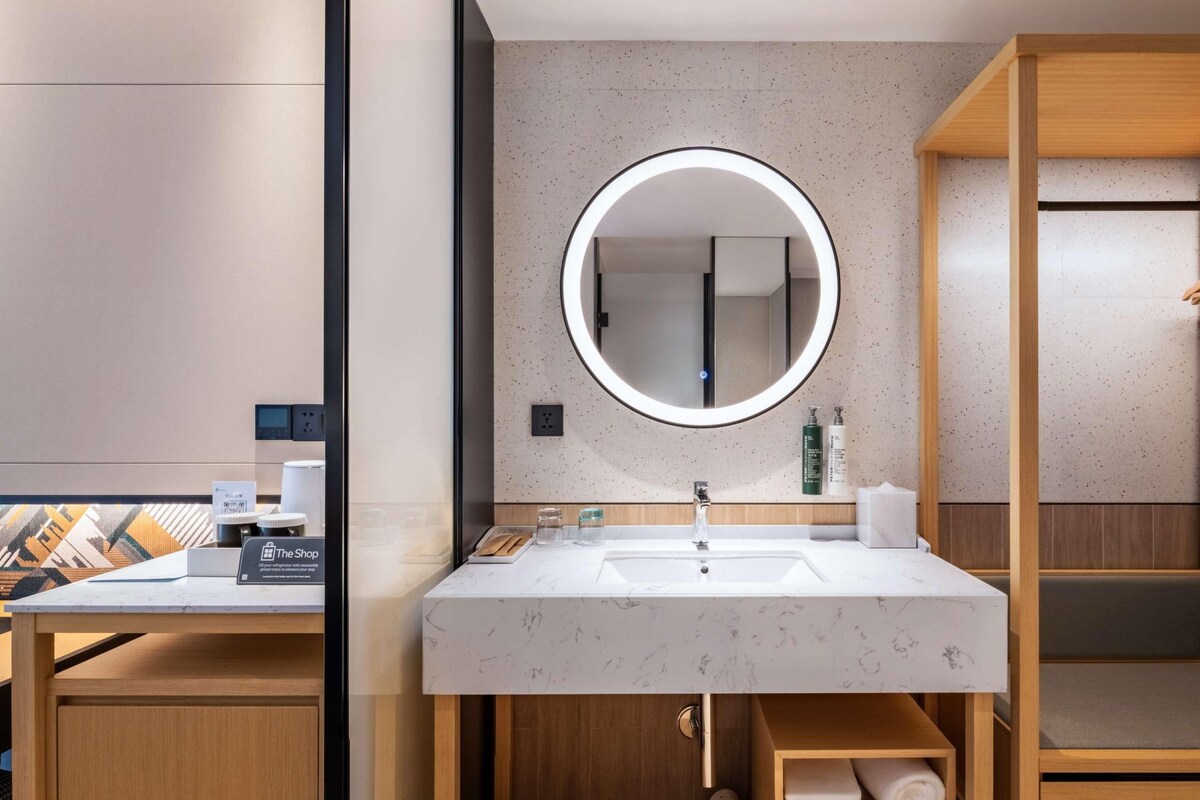 Une salle de bain moderne avec un lavabo en marbre, un miroir rond, des meubles en bois et un porte-serviettes.