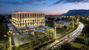 Een modern hotel met een rechthoekige structuur, verlichte ramen en een aangelegde omgeving met paden.