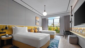 Een moderne hotelkamer met een bed, twee nachtkastjes, een bureau, een stoel, een televisie en een groot raam met uitzicht op gebouwen en bomen.