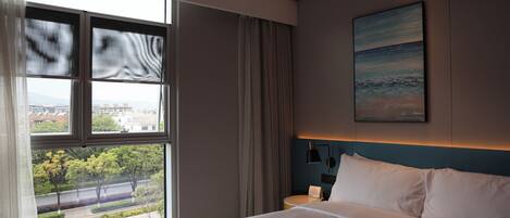 A hotel room with a large window, a bed, a nightstand, and a painting on the wall.