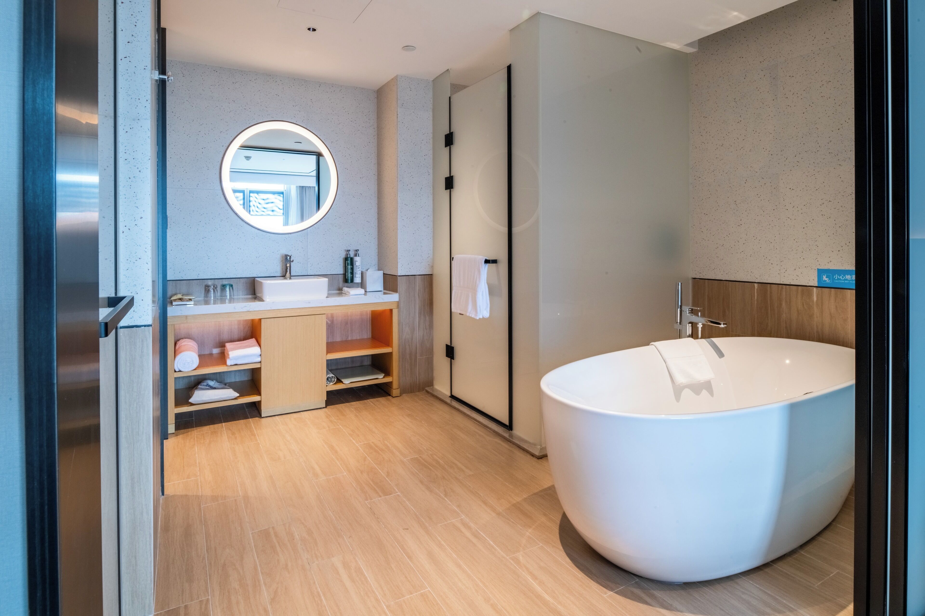 A modern bathroom with a freestanding bathtub, a round mirror, and a wooden vanity.