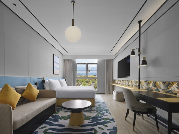 Una habitación de hotel moderna con cama, sofá, escritorio y un ventanal con vistas a la ciudad.