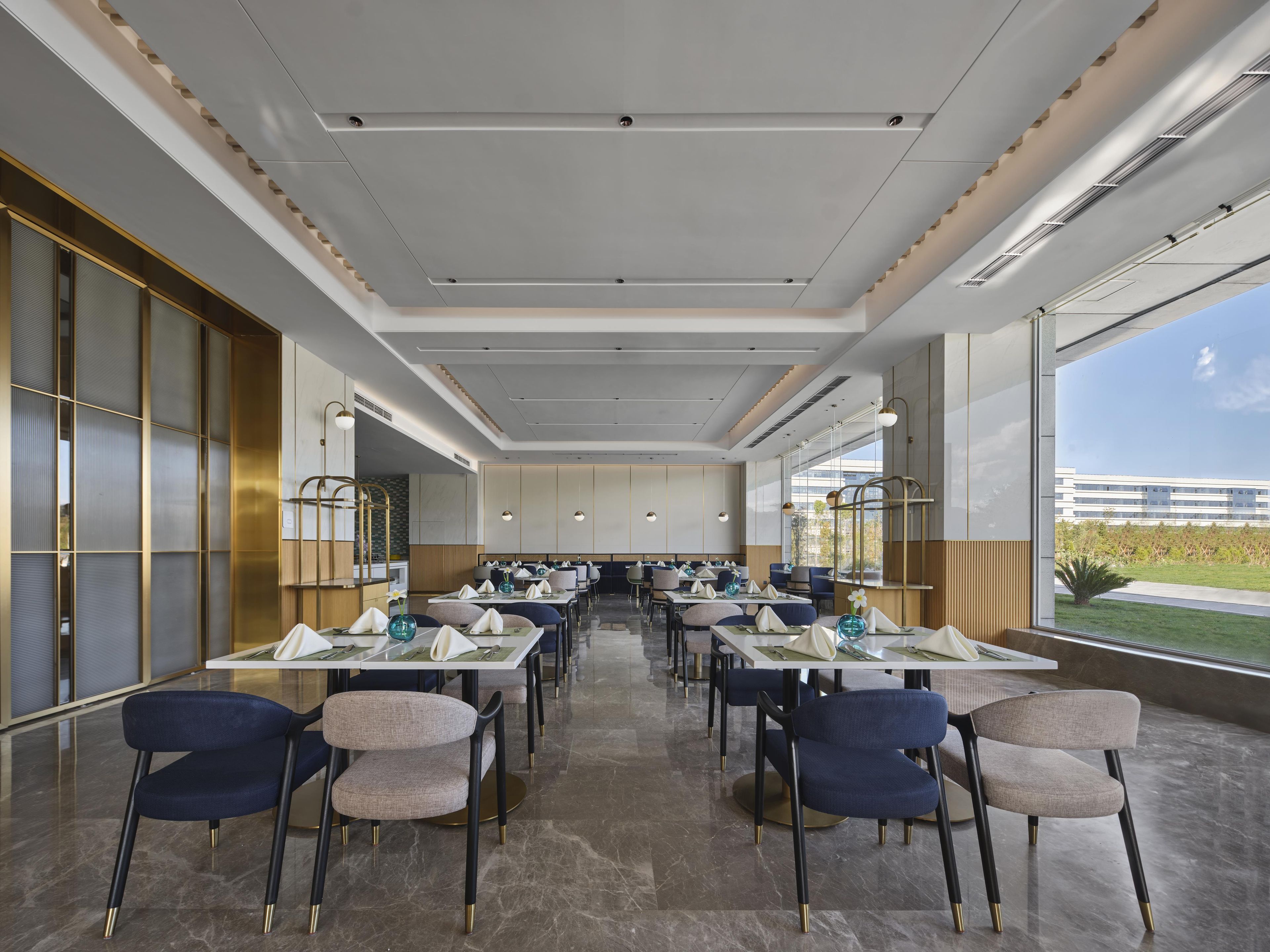 A modern dining area with tables and chairs, large windows, and a view of the outside.