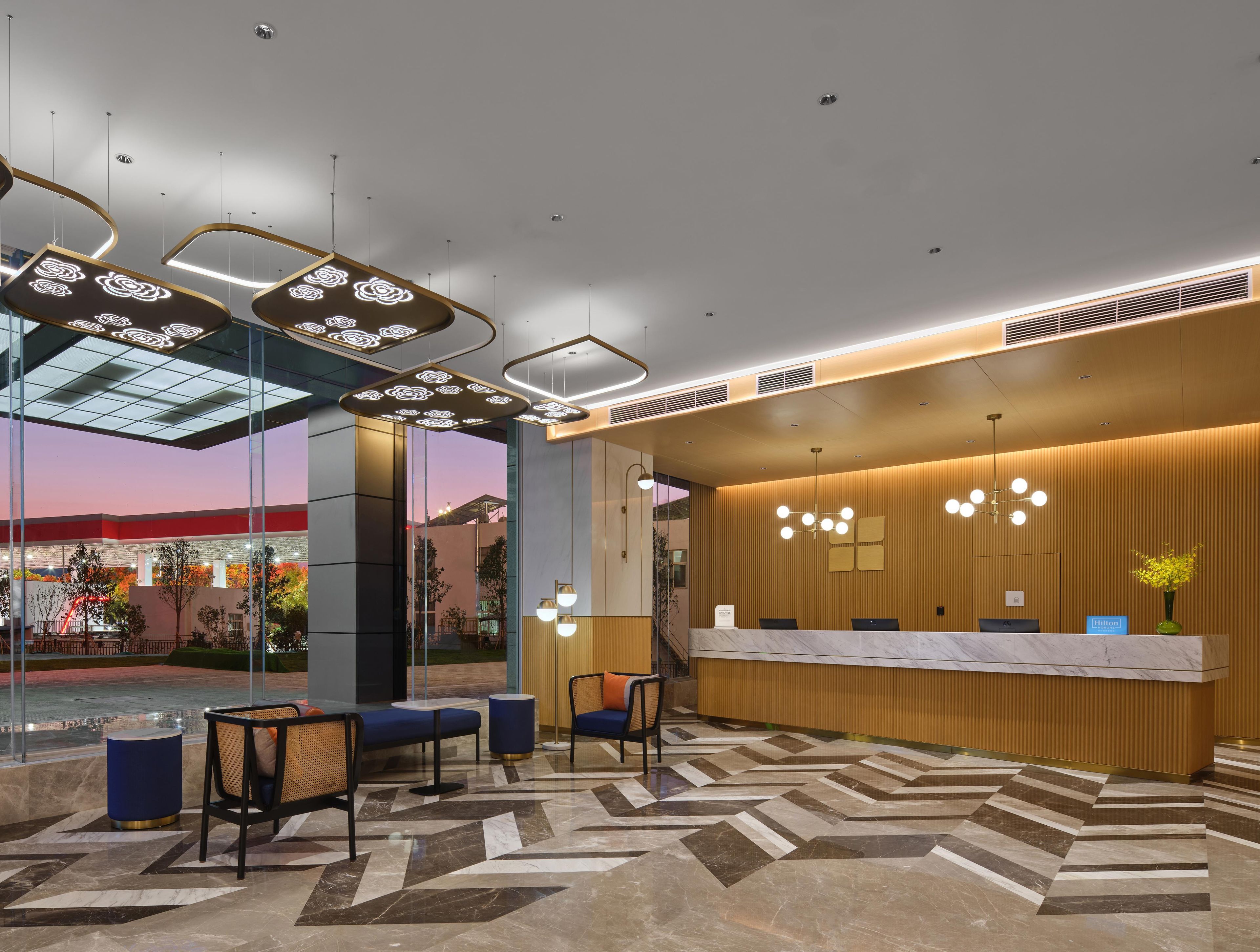 Un espace d’accueil d’hôtel au design moderne, comprenant un comptoir d’accueil, un coin salon et une vue sur l’extérieur.