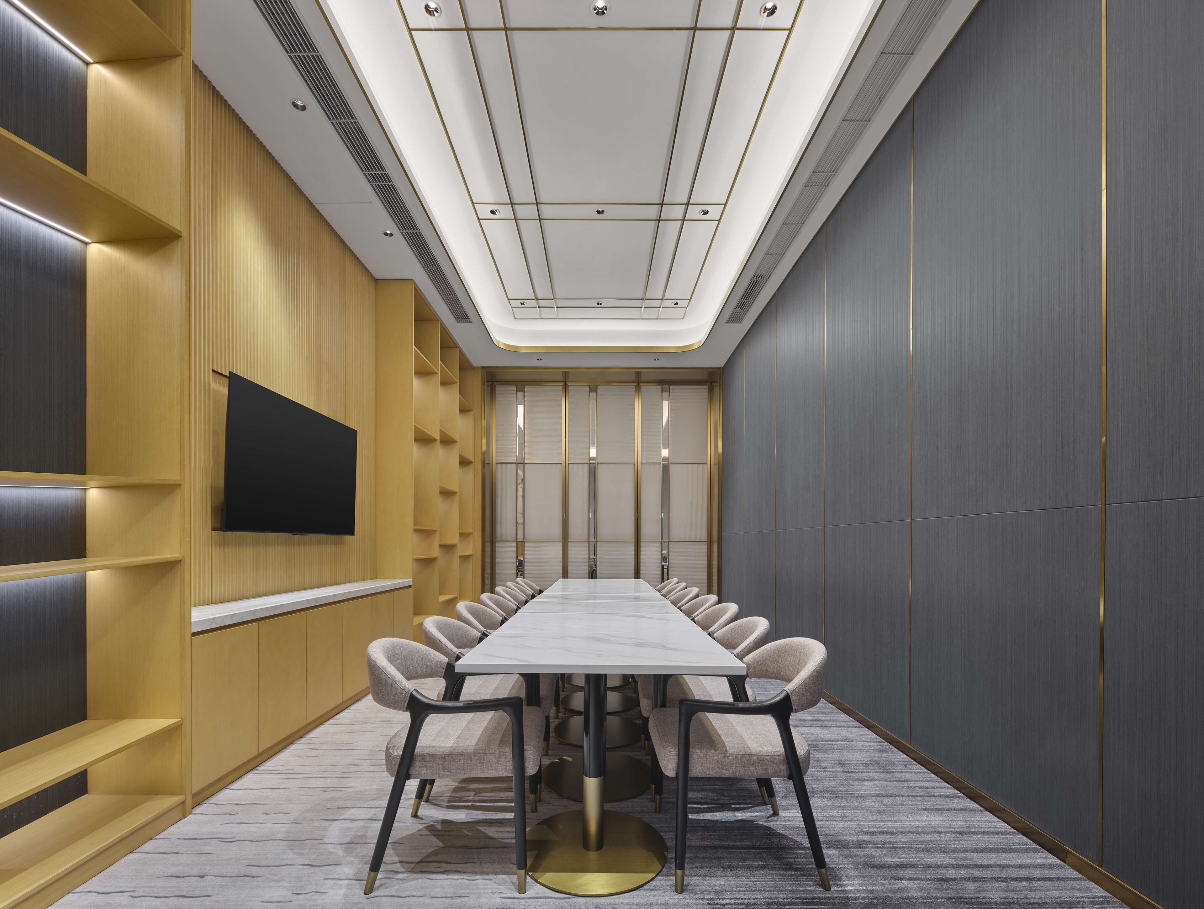 A conference room with a long table, chairs, a flat-screen TV, and a modern ceiling design.