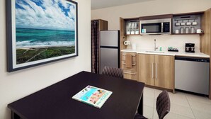 Una cocina moderna con microondas, cafetera y lavavajillas. En la pared, un cuadro enmarco con una escena de playa.