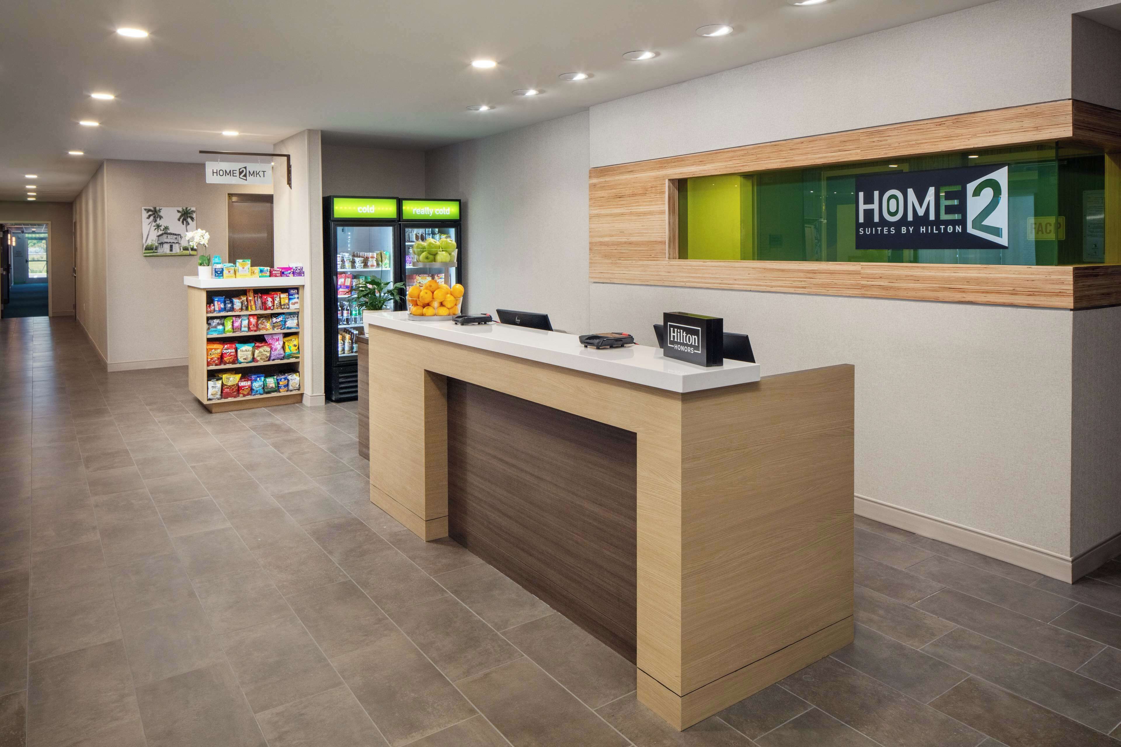 A hotel reception area with a reception desk, a vending machine, and a sign for 'HOME 2 Suites by Hilton'.