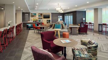 A modern hotel lobby with a bar, seating areas, and a television.