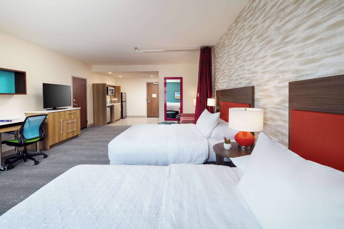 A hotel room with two beds, a desk with a chair, a TV, and a microwave.