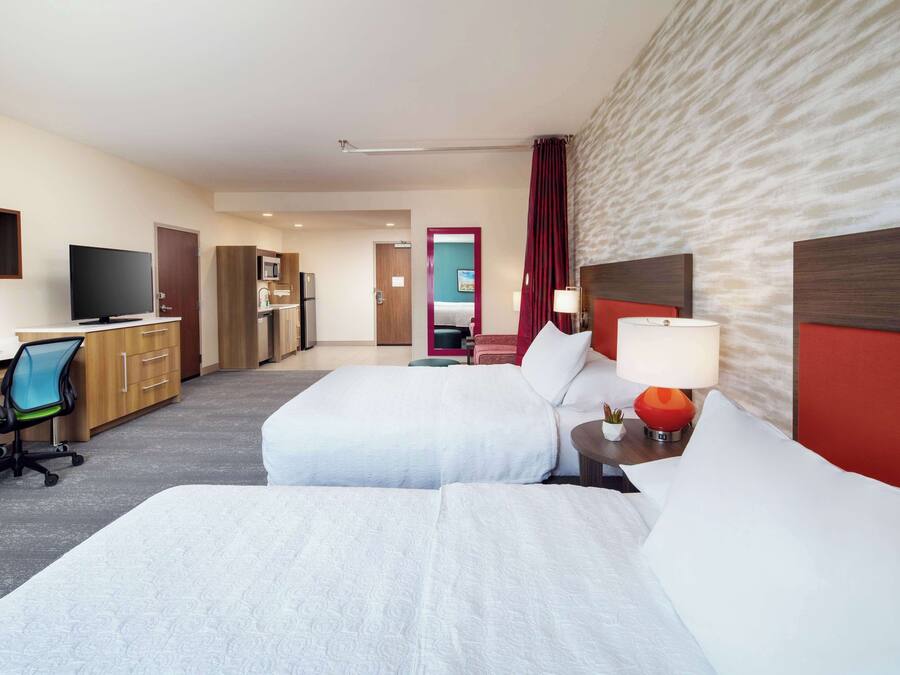 A hotel room with two beds, a desk with a chair, a TV, and a microwave.