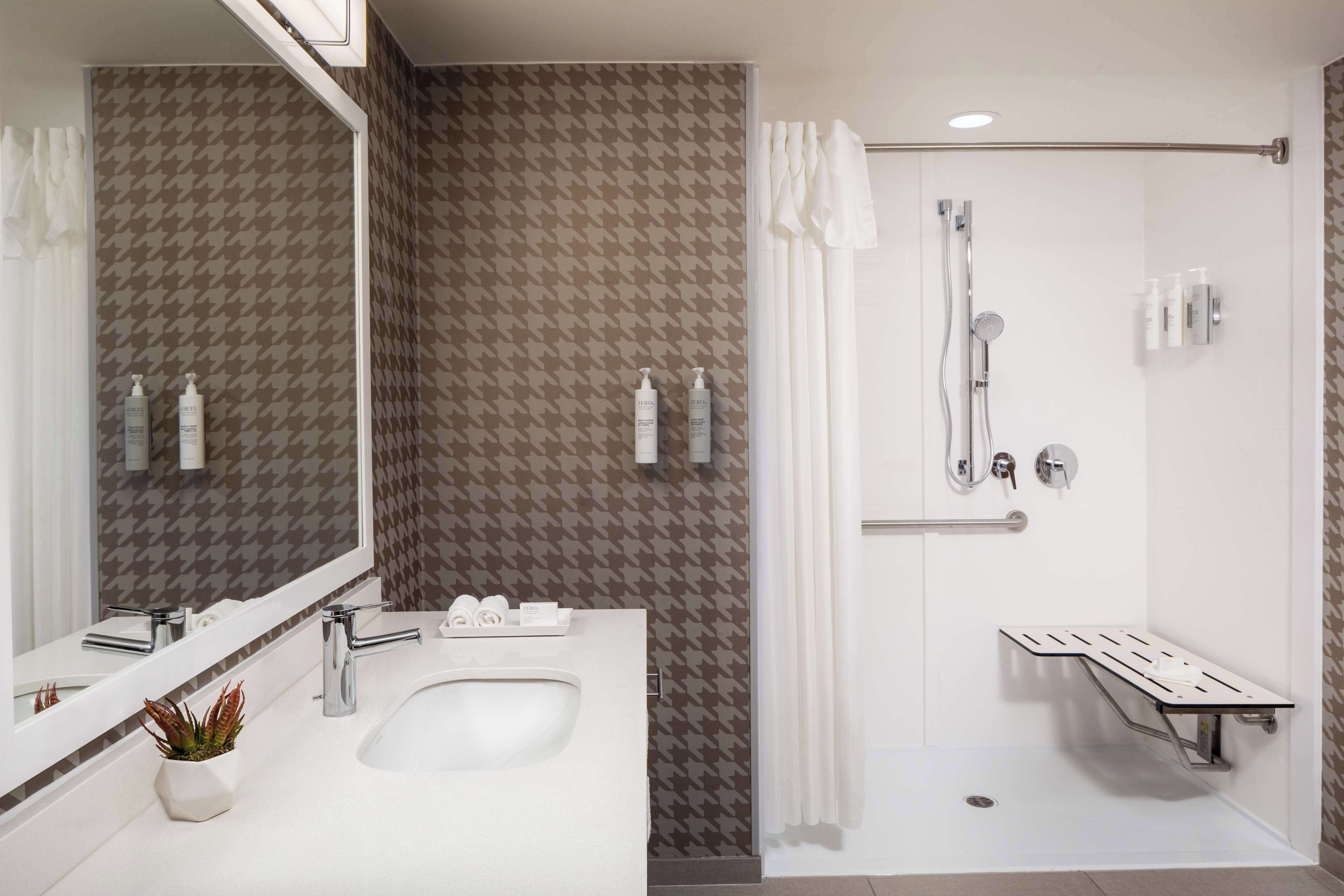 Een moderne badkamer met een witte wastafel, twee spiegels, een douche met een greep en betegelde wanden.