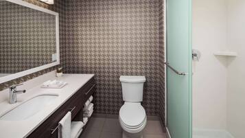Et badeværelse med en hvid vask, spejl og toilet, samt et bruseområde med glasdør.