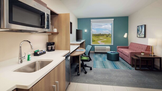 A modern kitchen with a built-in microwave, a sink, and a dining area with a table and chairs. There is a window with a view of a landscape. - Home2 Suites By Hilton Lake Mary Orlando (Lake Mary)