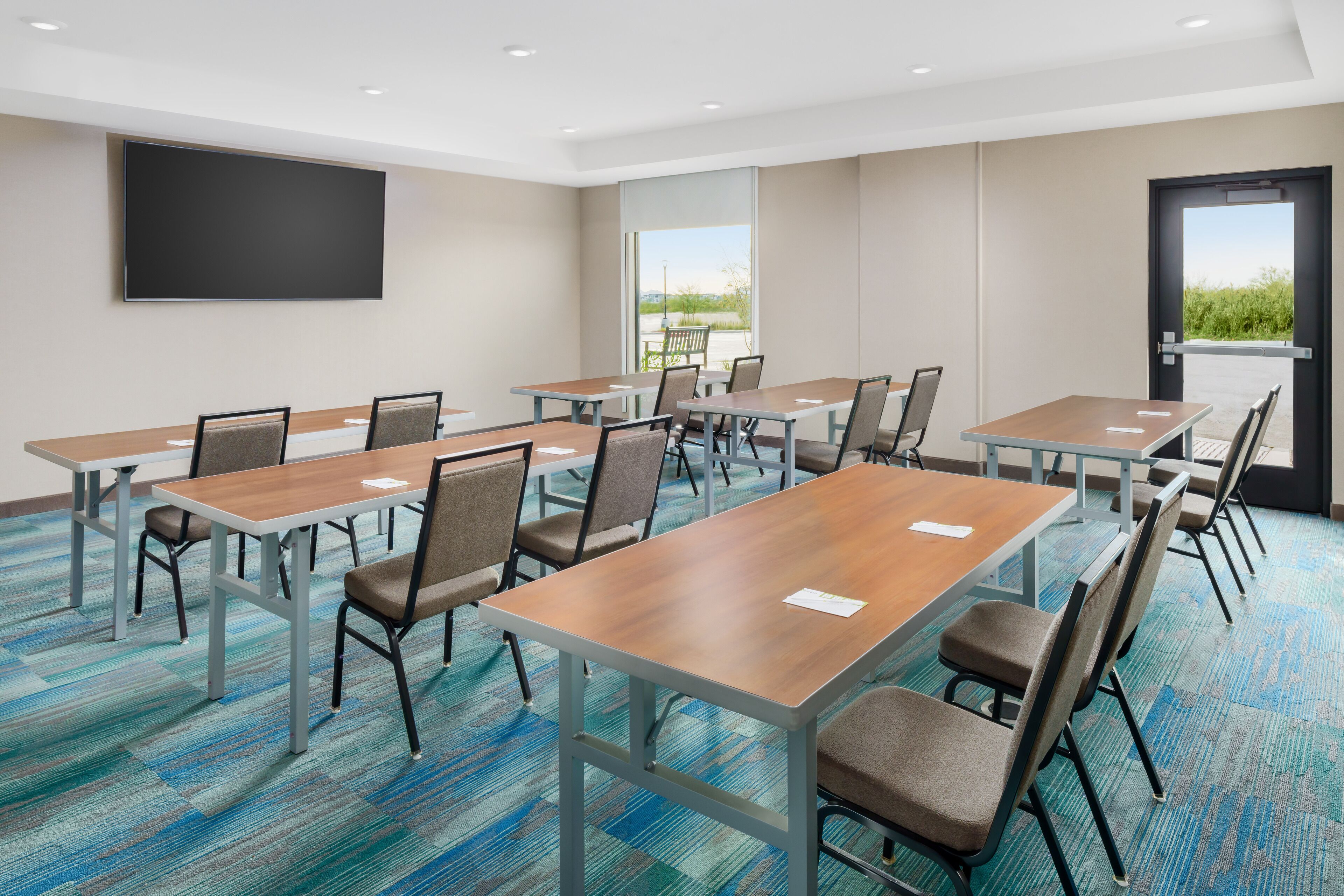 A conference room with multiple tables and chairs, a large flat-screen TV on the wall, and a door leading outside.