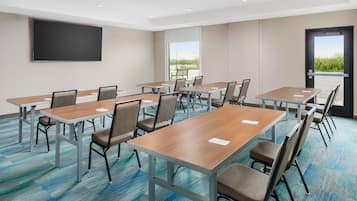 A conference room with multiple tables and chairs, a large flat-screen TV on the wall, and a door leading outside.